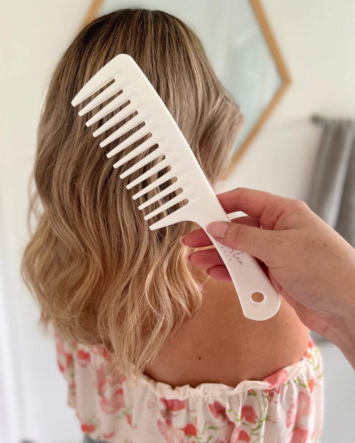 Wavy blonde hair being detangled with a white wide-tooth comb by a hand.