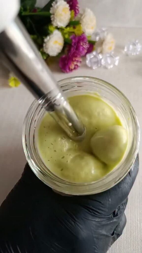 Green creamy hair mask in a glass jar being stirred with a metal tool