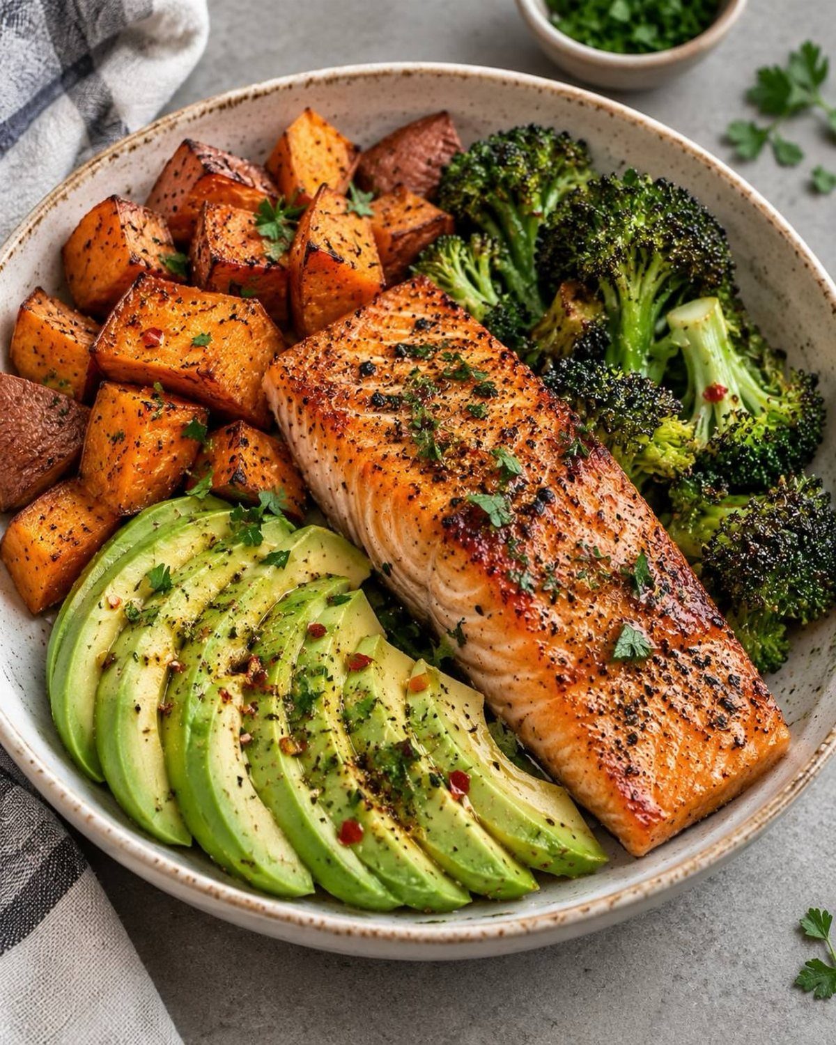 Cooked salmon fillet with sliced avocado, roasted sweet potatoes, and broccoli in a bowl.