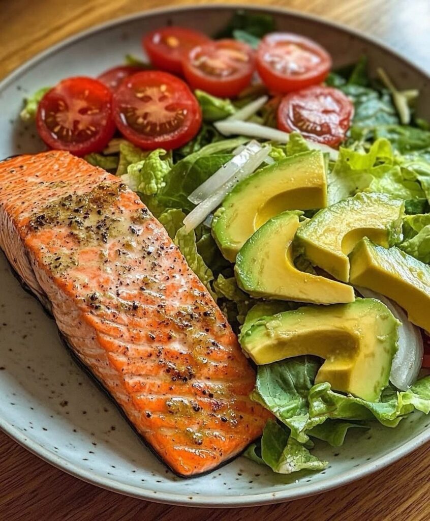 Cooked salmon fillet with sliced avocado and cherry tomatoes on a bed of lettuce