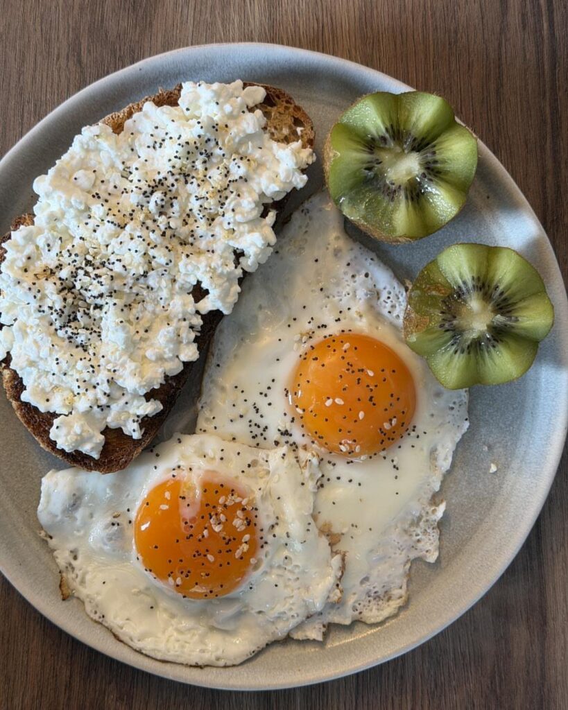 Two fried eggs, cottage cheese toast, and kiwi slices on a grey plate.