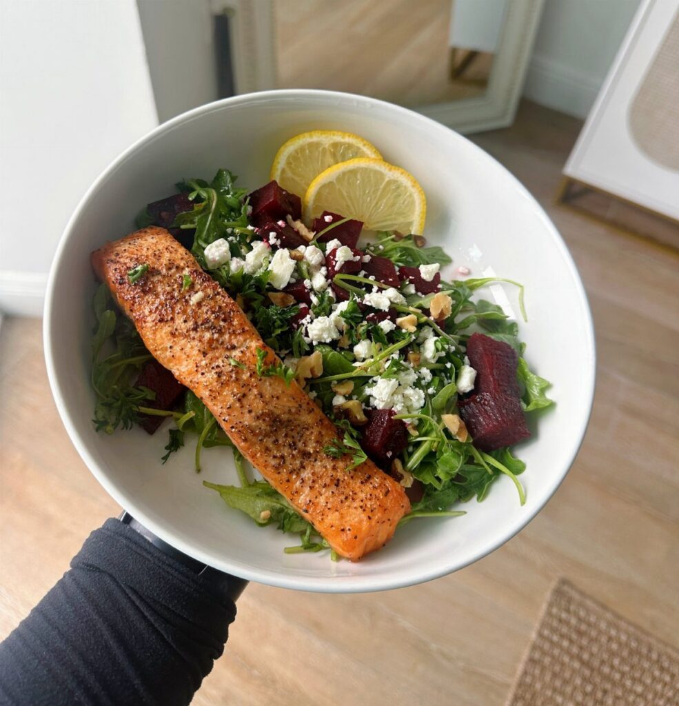 Cooked salmon fillet on a bed of leafy greens, beets, and feta cheese.