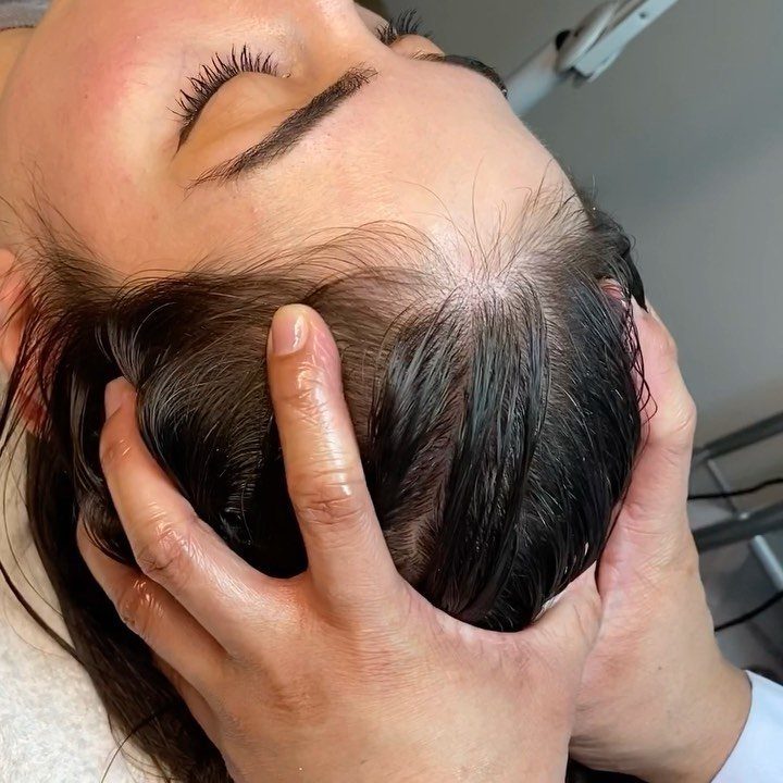 Hands massaging the scalp of a person with dark hair and closed eyes.