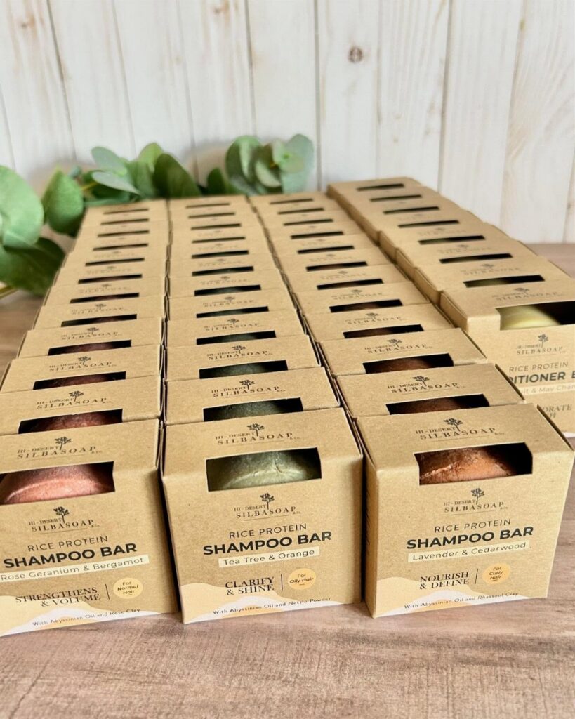 Brown cardboard boxes containing solid rice protein shampoo bars on a wooden surface.