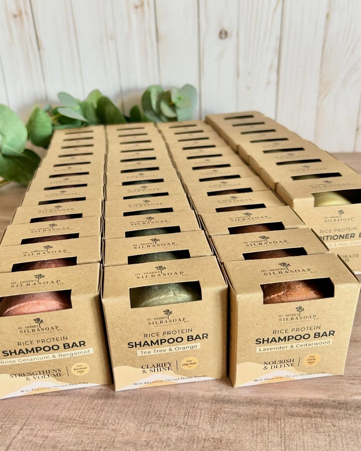 Brown cardboard boxes containing solid rice protein shampoo bars on a wooden surface.