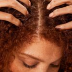 Person with curly red hair receiving a scalp massage along the center part.