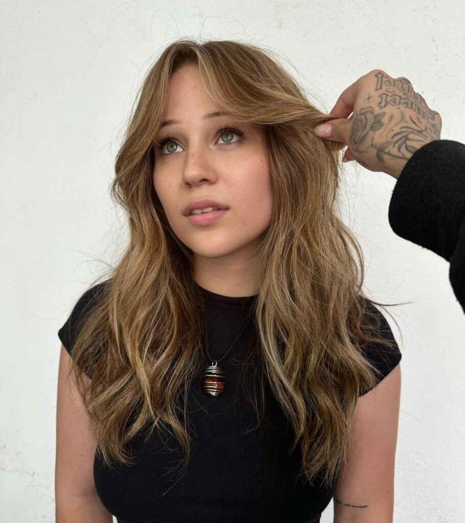 Woman with long light brown wavy hair and curtain bangs being styled.